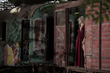 Attractive woman fashion model posing in the train wagon in the abandoned Red Star graveyard