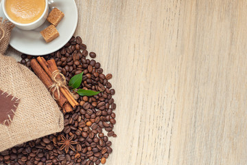 Cup with espresso with coffee beans, burlap sack and cinnamon on light wooden background