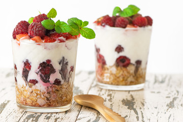 yogurt with muesli and berries in two glasses on light wooden table