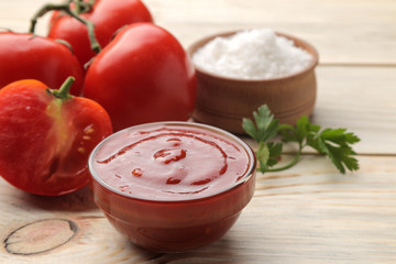 Red sauce in a bowl closeup with fresh tomatoes on a natural wooden table.