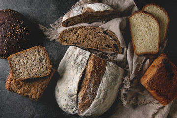 Variety of fresh baked rye, spelled, wheat craft artisan bread, whole and sliced, on cloth over...