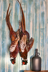 Fototapeta premium A pair of Male Pheasants and boottle on a old wooden background. Hunting season. Copy paste. Full size