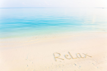 Fototapeta na wymiar The Word Relax Written in the Sand on a Beach with morning sea background