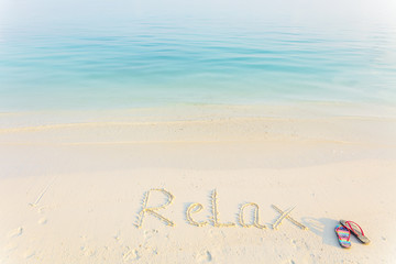 The Word Relax Written in the Sand on a Beach with flup flops at morning sea background