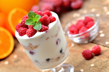 Yogurt with oatmeal and fresh raspberries in a glass, mint leaves, oranges and grapes in background