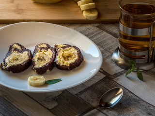 Banana cake with chocolate sauce and cup of tea on a white plate with wooden background