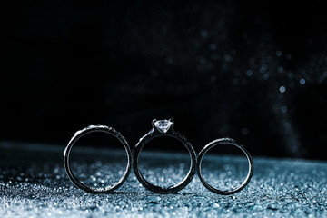 Fototapeta na wymiar three wedding rings dark background with copy space. Shiny water drops like fog