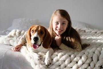 Cute child resting with beagle dog on the sofa. Beagle and girl looking at the camera together....