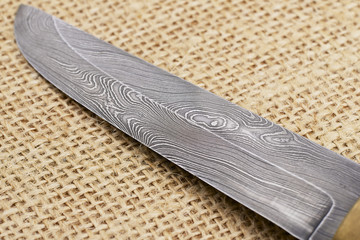 Traditional handmade Finnish knife with the abstract wave pattern of damascus steel over an old sack background. © Dmitry Chulov