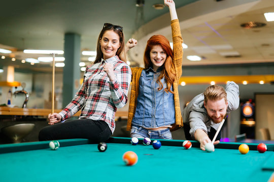 Happy friends enjoying playing pool