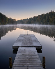 Scenic and idyllic lake landscape with pier and fog at autumn morning in Finland