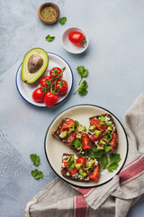 Avocados, cherry tomatoes and feta cheese sandwiches with balsamic sauce and cilantro on old olive board. Top view.