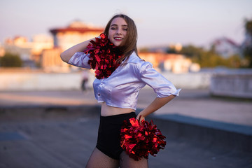 cheerleader with pompoms dancing outdoors on the roof at sunset
