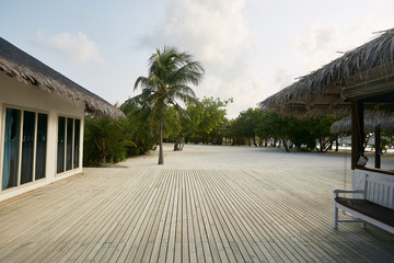 Large natural wooden floor terrace at tropical island with palm trees and bungalows on background, space for text or product lay. Advertising concept.