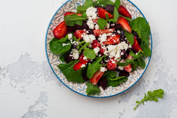 Beets, strawberries, feta cheese and arugula salad in ceramic plate on old concrete table background. Top view.