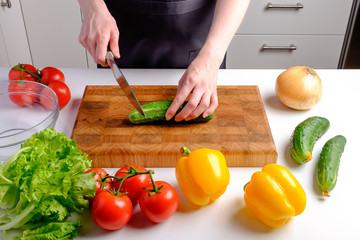 Woman cutting fresh cucumber on wooden board ingredients for salad