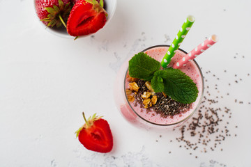 Pink strawberries, banana smoothie with granola and chia seeds in glass on light white concrete background. Top view. Copy space.