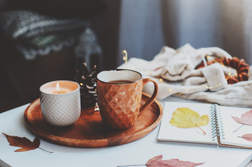 cozy autumn or winter morning at home. Still life details with cup of tea, candle, sketch book with herbarium and warm sweater. Scandinavian hygge concept