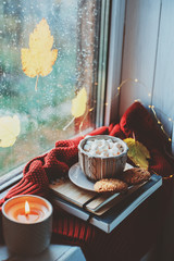 cozy autumn morning at home. Hot cocoa with marshmallows and candle on window in rainy cold day. Spending holidays at home.