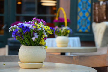 Decorative composition of multicolored wildflowers in vase on the table of street cafe.