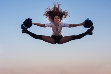 Cheerleader girl with pompoms performs acrobatic element outdoors on the roof