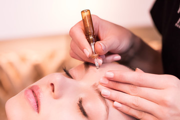 Closeup of a beautician applying a skin care serum ampoule on a pretty woman.