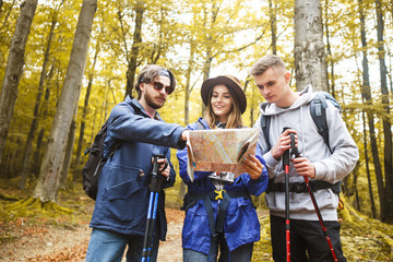 Young hiking friends holding map and searching some places together in the forest