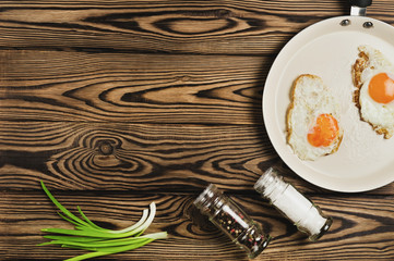 Two fried eggs in metal beige pan near spices on old wooden brown table. Top view with copy space