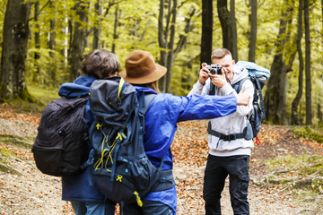 Group of friends on country walk on a sunny day, young people hiking in countryside, blonde boy making photo to his friends, travelling concept