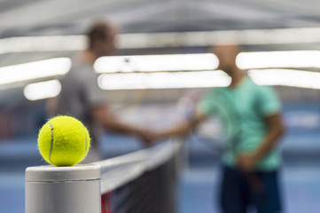 Tennis ball on tennis net, players shaking hands in background