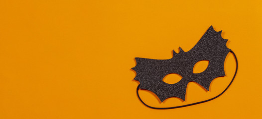 Black halloween mask on orange background
