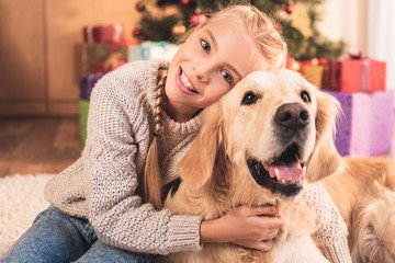 smiling kid hugging golden retriever dog and sitting near christmas tree