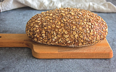 Multi-grain healthy bread. Delicious homemade bread with seeds and whole grains on a wooden board against a dark background. Close-up.