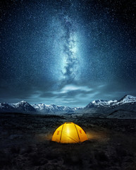 Kamperen in de wildernis. Een opgezette tent onder de gloeiende sterren van de nachthemel van de Melkweg met besneeuwde bergen op de achtergrond. Natuur landschap foto composiet.