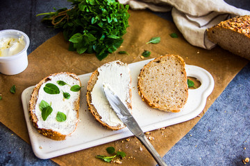  Fresh bread sandwich with soft cheese and herbs on pergamete paper on a stone table. Delicious breakfast sandwich. Culinary background.