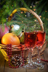 Fototapeta na wymiar Basket with oranges and New Year toys and decoration, glasses of wine in front and New Year tree on background