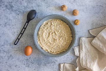 The dough for the pie. Raw dough for pie in a baking dish on a dark background, next to a towel, rolling pin and nuts. Cake baking recipe, save the space, top view