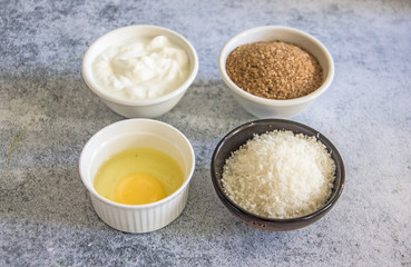 Ingredients for baking - raw egg, flour, brown sugar, nuts, soft cheese on a stone background