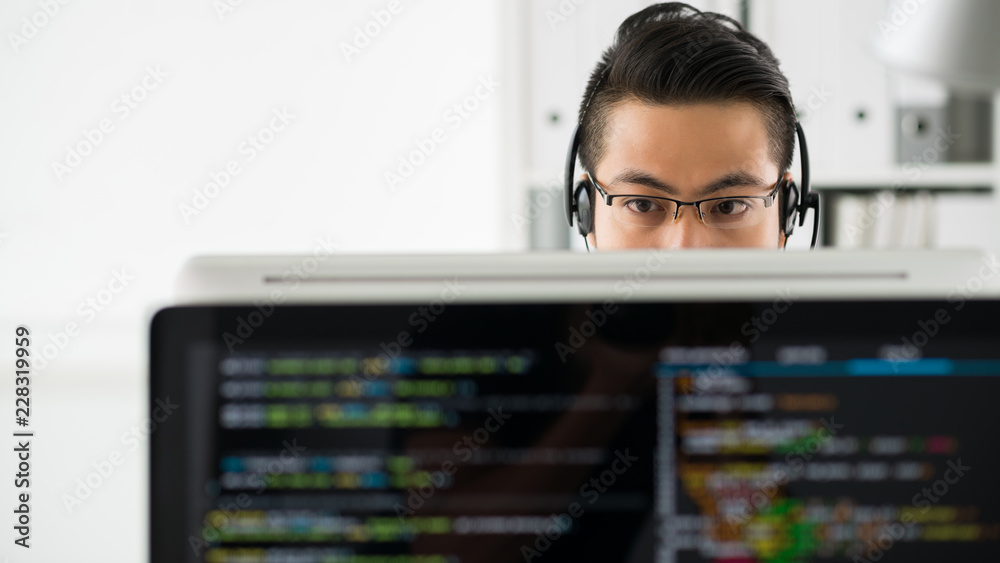 Wall mural young asian man in headset and glasses working with computer and programming