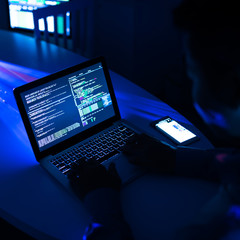 Crop shot of man using laptop and hacking security system sitting in neon glowing darkness