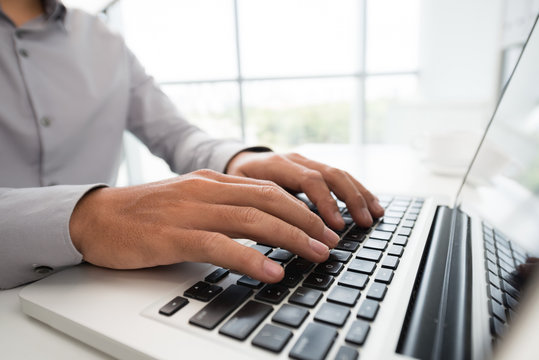Crop side view of formal man typing on laptop while coding in modern light office