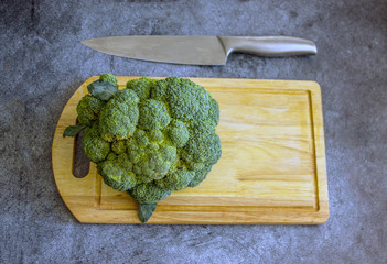 Big head of cabbage of fresh broccoli cabbage on a wooden board on a dark table, near a knife, top view