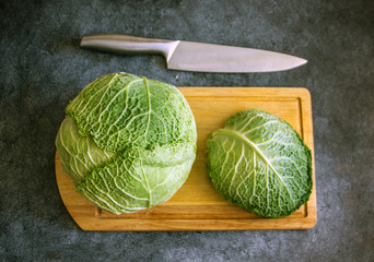 Big swing of savoy cabbage on a cutting board near a knife on a dark table, top view