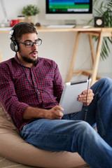 Young man in eyeglasses wearing headphones looking at tablet screen and singing song