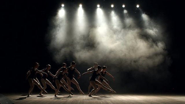 A group of flexible girls ballet dancers dancing on stage on a black background, slow motion. Young children dancing ballet. Ballet.