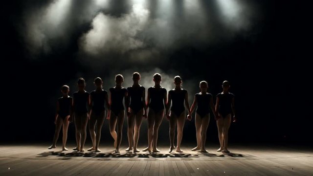 A very large group of children perform and dance on stage in the dark with smoke and concert lighting, they simultaneously bow at the end of the performance. Dancing. Ballet.