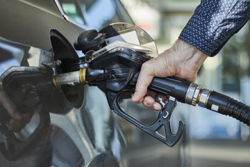 Closeup of a hand filling a fuel tank of a car with fuel dispenser in petrol station.
