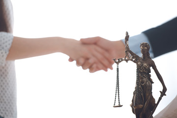close-up view of lady justice statue and lawyer with client blank shaking hands behind