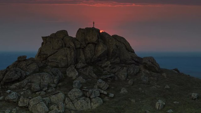 Sunset beyond a mountain with a cross on top. Beautiful panorama of a roumanian mountains landscape. Time lapse