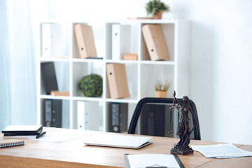 lady justice statue, papers and laptop on table in office
